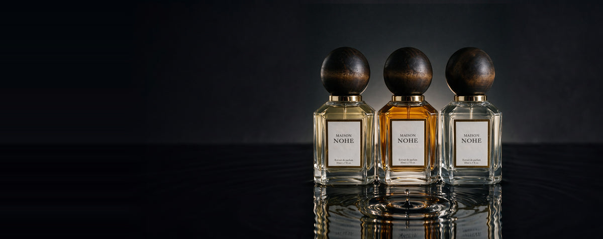 Trois flacons Maison Nohe sur un miroir d'eau noire